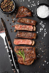 Closeup ready to eat steak new York beef breeds of black Angus with herbs, garlic and butter on a stone Board. The finished dish for dinner on a dark stone background. Top view