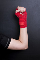 Female hand in a bandage with red boxing tape is raised upwards as a symbol of the struggle for rights. Fight like a girl