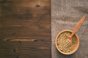 Malt grains in wooden bowl with spoon on burlap cloth on brown wooden table background with copy space.