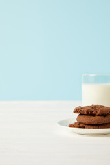 chocolate cookies on saucer and milk glass on blue background