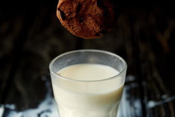 closeup view of chocolate cookie falling into glass with milk