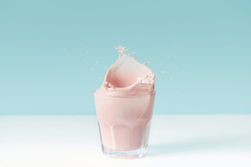 splashing drops of strawberry milkshake from glass on blue background