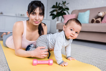 young happy mother and little child on yoga mat at home looking at camera