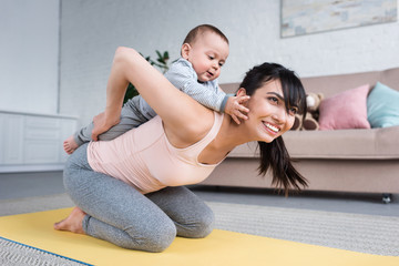 Fototapeta na wymiar little child piggybacking on mother while she standing on yoga mat at home