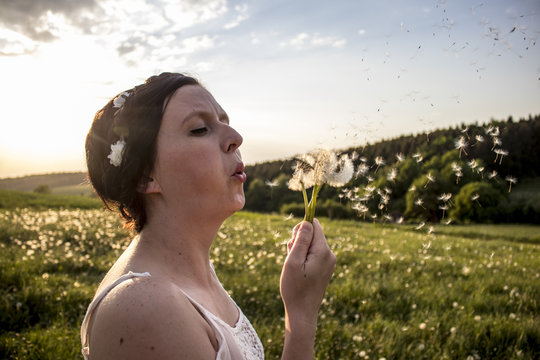Young woman blows dandelion flower
