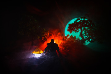 Man in raincoat coming from dark forest with glowing lantern in his hand concept. Silhouette of a horror killer with lamp