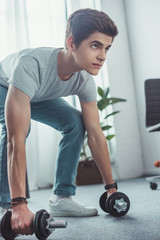 handsome teenager squatting with dumbbells at home