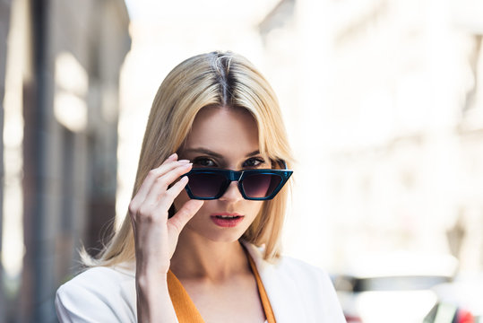 portrait of beautiful young blonde woman adjusting sunglasses and looking at camera