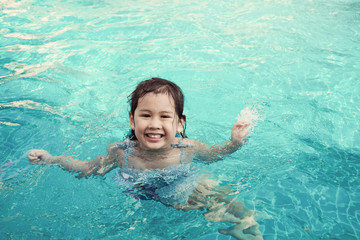 Happy little asian girl having fun in swimming pool in summer