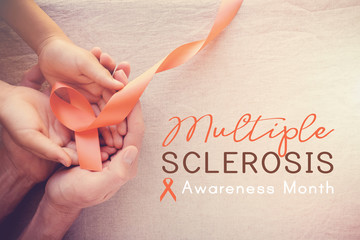 Adult and child hands holding orange Ribbons,  Multiple sclerosis awareness month - obrazy, fototapety, plakaty