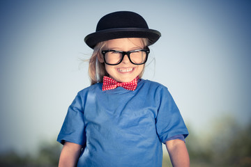 Outdoor portrait of funny happy little girl in bow tie and bowler hat. Retro stile.