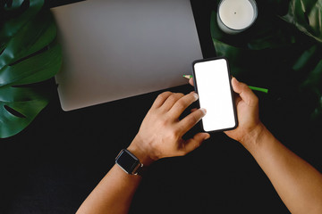 Man using mobile phone  on office dark leather desk table with supplies and coffee cup