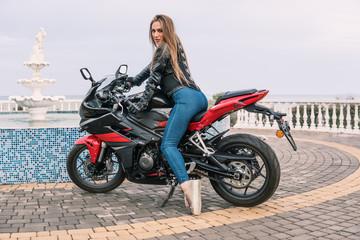 Naklejka na ściany i meble Biker girl in a leather jacket on a black and red color motorcycle.
