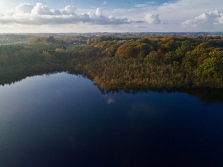 Aerial view over lake in Sweden with forest around with shade of brown and orange