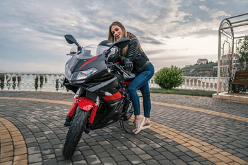 Fototapeta na wymiar Biker girl in a leather jacket on a black and red color motorcycle.
