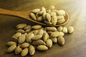 Almonds seeds pour from wood spoon on textured wooden background, top view.