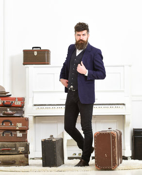 Man, traveller with beard and mustache with luggage, luxury white interior background. Macho elegant on strict face standing near pile of vintage suitcase. Luggage and travelling concept.