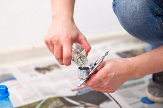 Close-up of a woman artist in jeans and sneakers washed with water and prepares a metal airbrush for work before painting the walls in the children's room