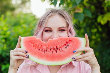 Beautiful young woman with pink hair holding juicy watermelon close to the face