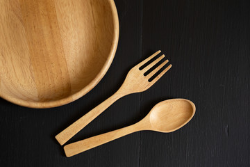 Spoons, forks and Dish made of wood on the black wooden background