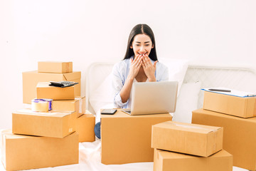 Young woman freelancer working and use laptop computer with cardboard box on bed at home - SME business online and delivery concept