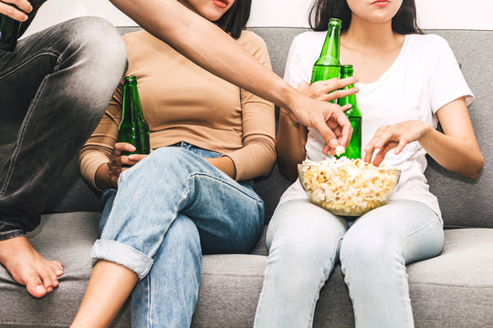 Group of friends eating popcorn and drinking beer together and watching tv on sofa at home.Friendship and party concept