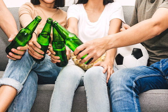 Group of friends eating popcorn and drinking beer together and watching soccer game on sofa at home.Friendship and party concept