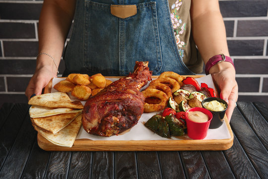 Hands holding plate with fried turkey thigh, grilled vegetables and snack for beer