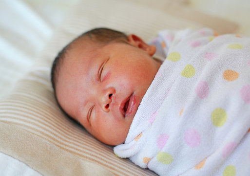 Portrait of newborn baby boy in a blanket lying on the bed.