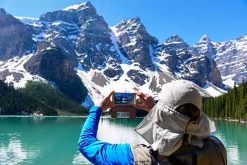 A Tourist enjoys taking picture by mobile phone of Valley of the Ten Peaks, Moraine Lake, Alberta,...