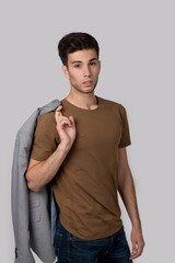 Portrait of a stylish young man wearing brown shirt and jeans on grey background in studio .