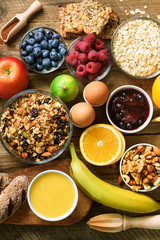 Healthy breakfast ingredients, food frame. Granola, egg, nuts, fruits, berries, toast, milk, yogurt, orange juice, cheese, banana, apple on wooden rustic background, top view, copy space.