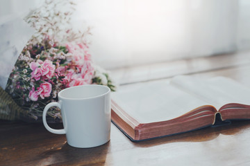 Holy bible with flowers on wooden table background against window light with copy space.