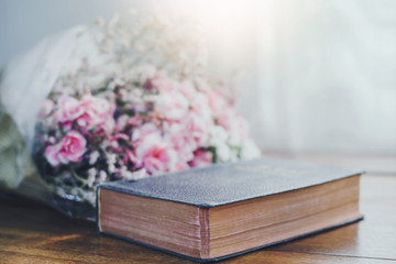 Holy bible with flowers on wooden table background against window light with copy space.