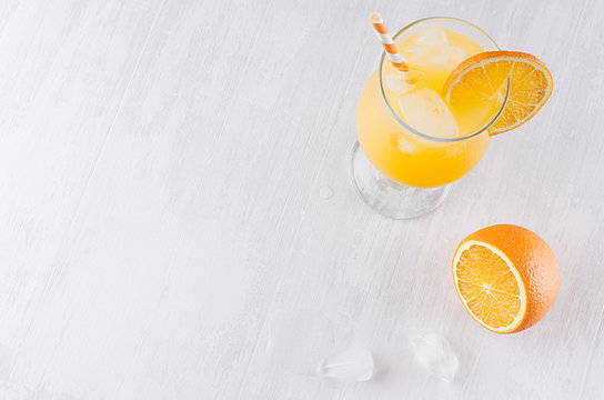 Colorful orange cool citrus cocktail with slice oranges, ice cube, straw on white modern wooden background, top view.