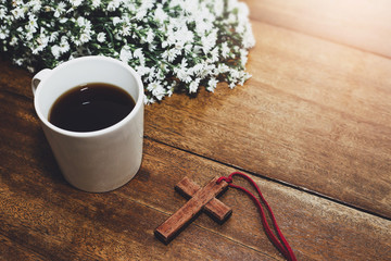 wooden cross with a cup of cup of coffee and flowers on wooden background
