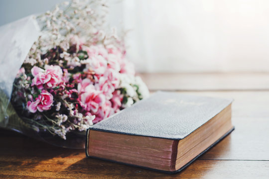 bible and flowers on wooden table against widow light