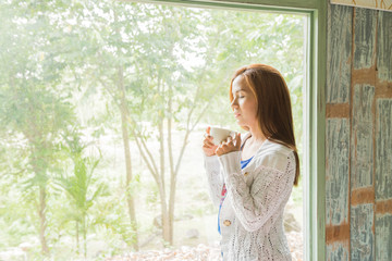 woman drinking coffee sitting by the window in the house.