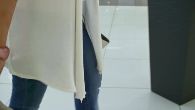 Side view of stylish smiling woman in scarf walking along shopping center hallway and looking around after buying clothes