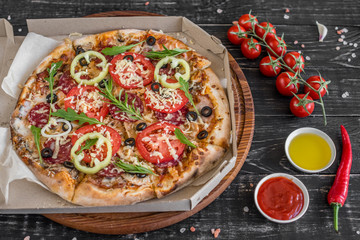 Vegetables, mushrooms and tomatoes pizza on a black wooden background. It can be used as a background