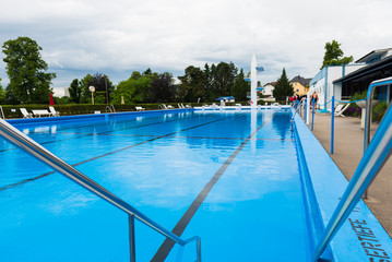 Blick über ein Schwimmbecken eines Freibades mit ruhigem Wasser vor der Öffnungszeit