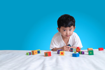 3 years old little cute Asian boy play toy or square block puzzle at home on the bed, kid lying learn by playing block shape or pieces, education and healthy concept idea.