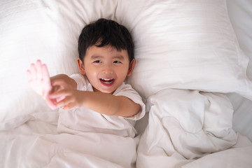 Obraz na płótnie Canvas 3 years old little cute Asian boy at home on the bed, kid lying playing and smiling on white bed with pillow and blanket, top view with copy space.