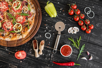 Vegetables, mushrooms and tomatoes pizza on a black wooden background. It can be used as a background