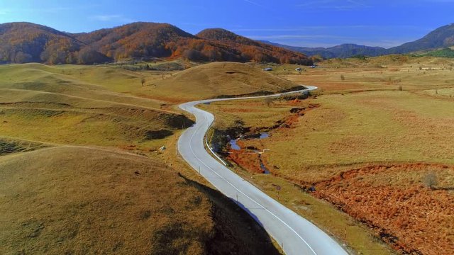 Aerial over autumn valley with flat hills and twisty paved road