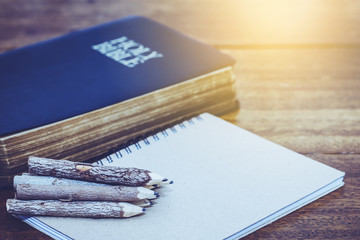stack of natural hand made pencils on small note book and the holy bible on wooden background