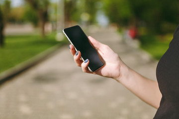Cropped close up of woman hands holding and using mobile phone, smartphone with blank empty screen in city park outdoors. Technology, communication concept. Copy space for advertisement.