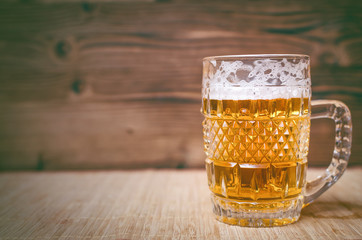 Glass of frothy light beer on the wooden table background. Front view. Alcohol background with copy space.