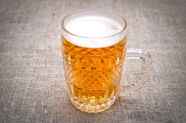 Glass of frothy light beer on the burlap cloth background.