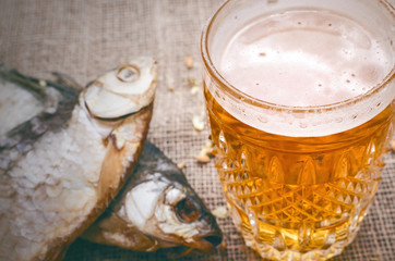 Glass of light beer and stockfish on burlap cloth background.